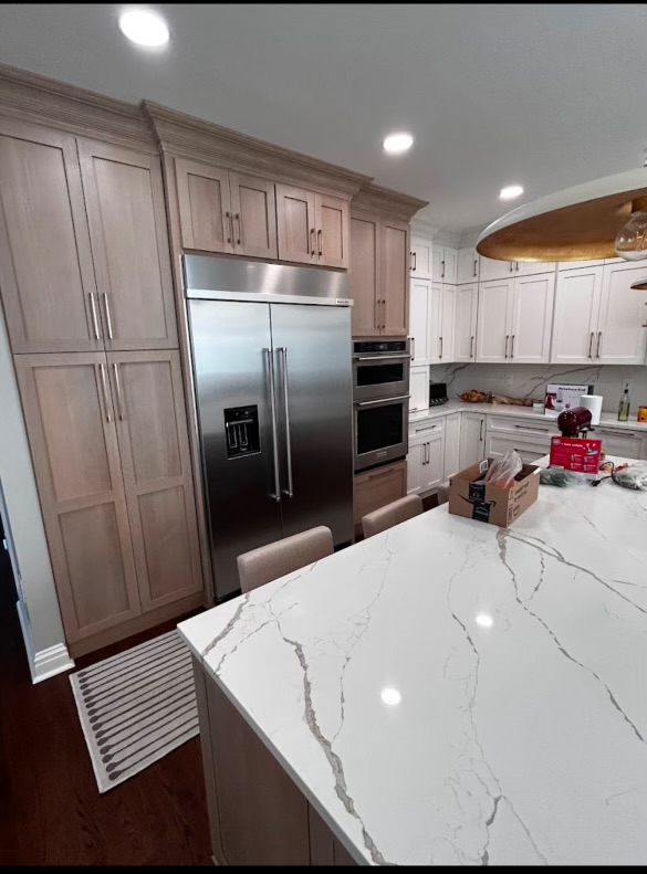 Built-in appliance wall with integrated ovens beside a stone-topped island in a custom luxury kitchen