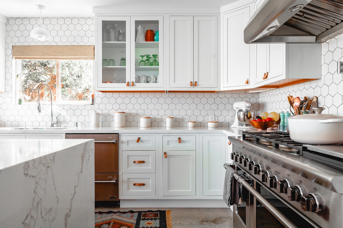 White kitchen with hex tile backsplash, marble waterfall island, and professional-grade range -- strategic splurges that maximize impact (Photo: Rustic Vegan / Unsplash)