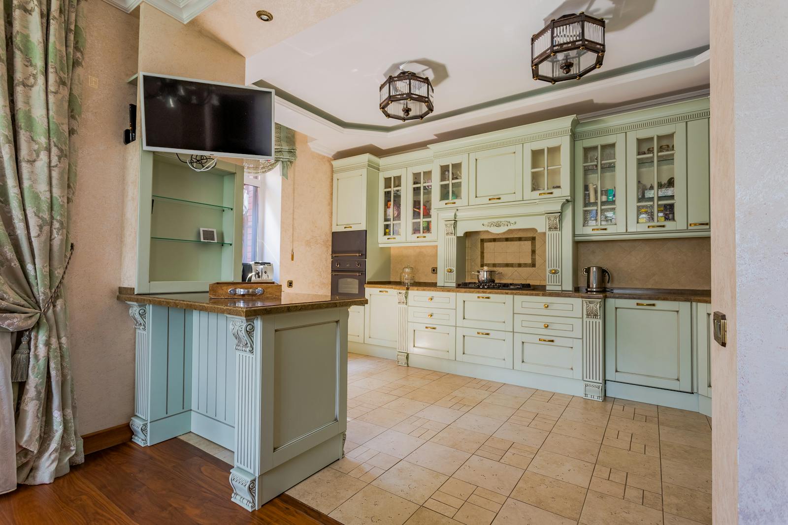 A full sage-green kitchen with glass-front uppers and warm hardware — proof that earthy green reads as a timeless, not trendy, choice