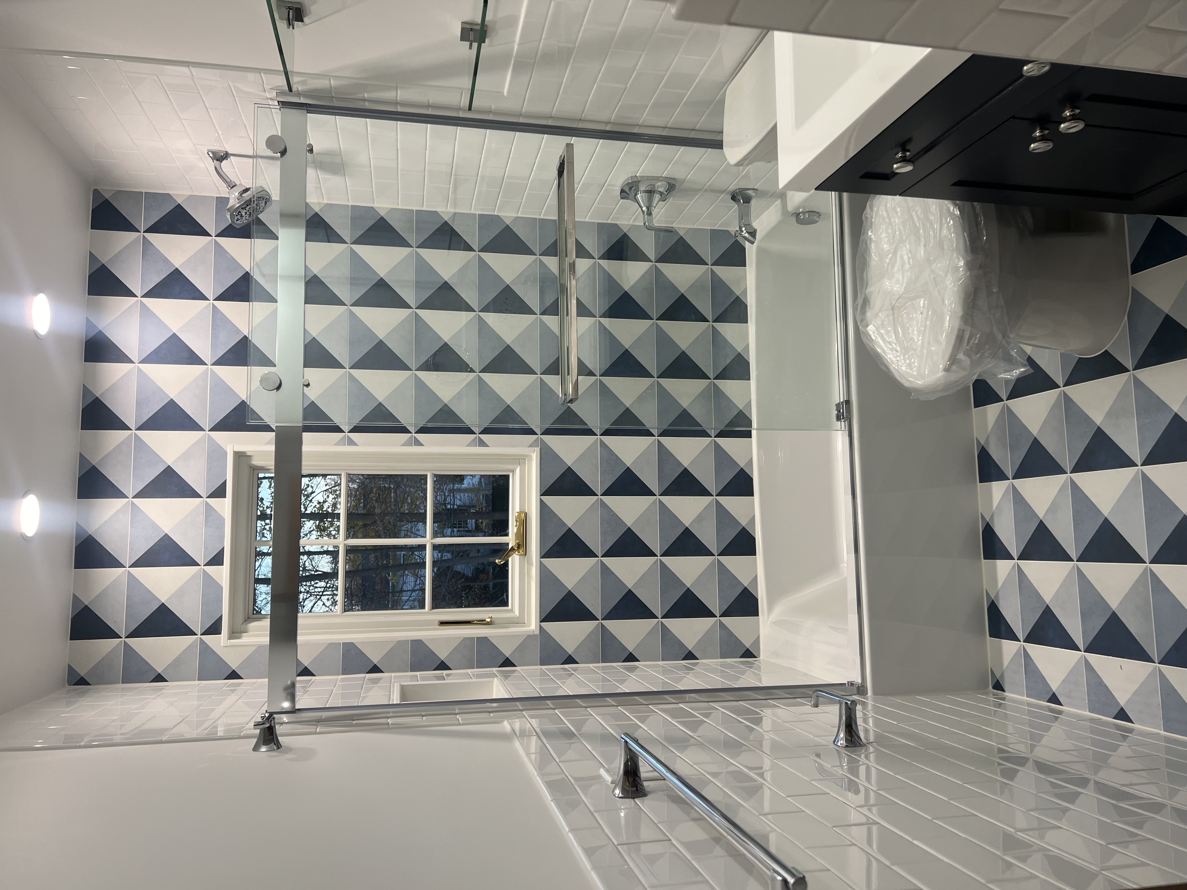 Bathroom with patterned blue and gray tub-surround tile, sliding glass enclosure, and dark vanity